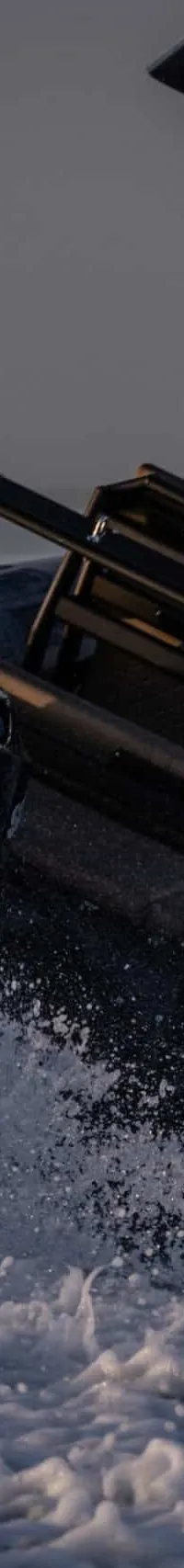 Een man in een blauwe jas bestuurt een zwarte BRIG-RIB met een Suzuki 200 pk buitenboordmotor, die door water vaart.