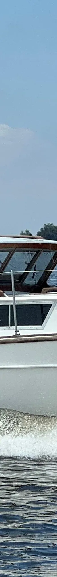 Een witte motorboot met de naam "Jenneke" vaart over water en creëert een boeggolf, met een Nederlandse vlag aan de…