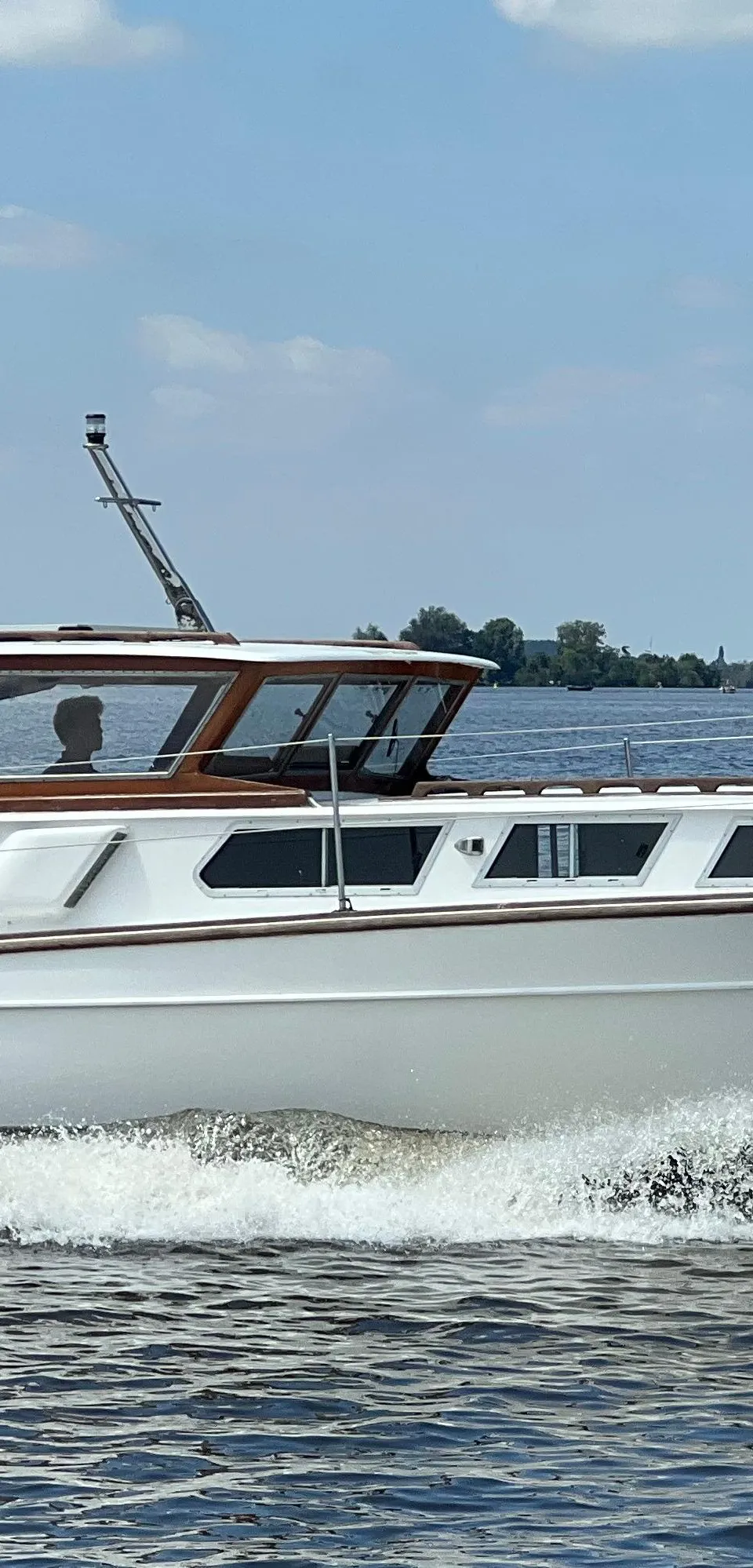 Een witte motorboot met de naam "Jenneke" vaart over water en creëert een boeggolf, met een Nederlandse vlag aan de…