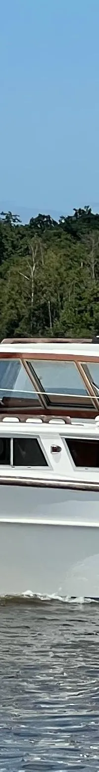 Een witte motorboot met de naam "Jenneke" vaart op het water, met een Nederlandse vlag aan de achterkant.