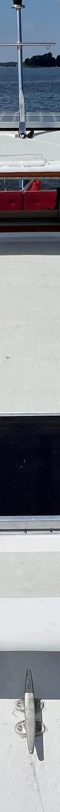 Een bovenaanzicht van een witte boot met een houten stuurhut en een luik op het voordek, varend op rustig water.