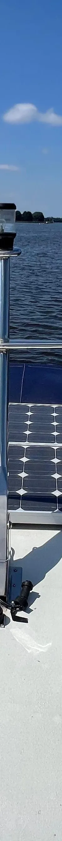 De foto toont de boeg van een boot met twee zonnepanelen en een navigatielicht, varend op een waterweg.