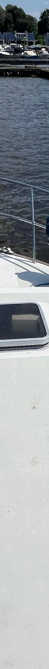 De foto toont de boeg van een boot met twee blauwe stootwillen, een reling en een luik, varend op donker water.