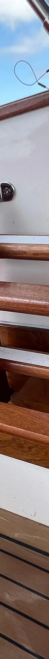 Een rood kussen met witte bies, een houten trapje, een luidspreker en een teakhouten vloer zijn zichtbaar.