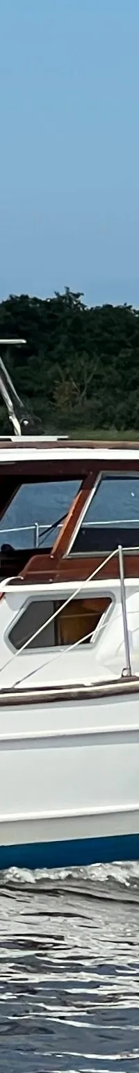 Een witte motorboot met blauwe kap en Nederlandse vlag vaart op het water, met "LOOSDRECHT" op de spiegel.