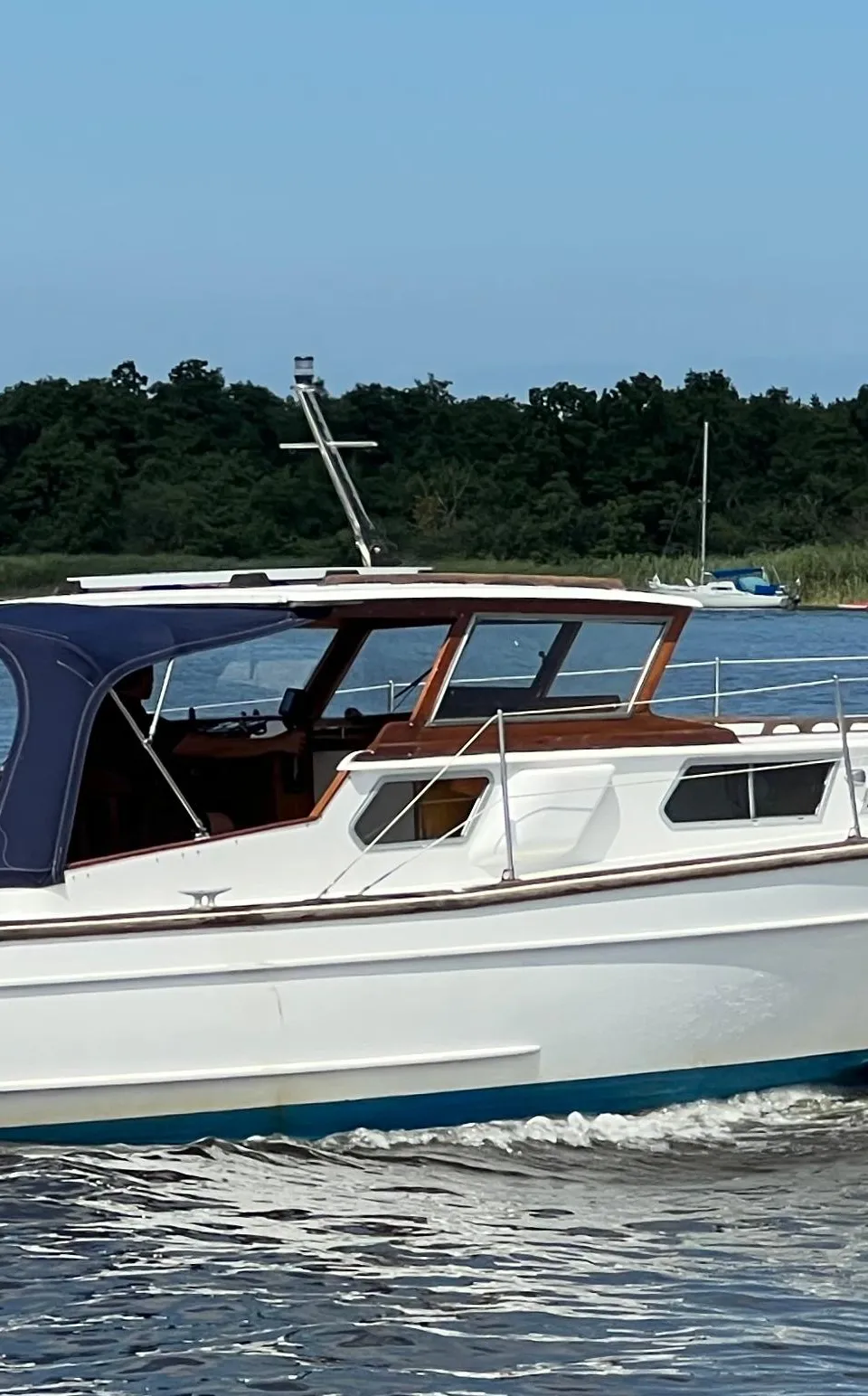 Een witte motorboot met blauwe kap en Nederlandse vlag vaart op het water, met "LOOSDRECHT" op de spiegel.