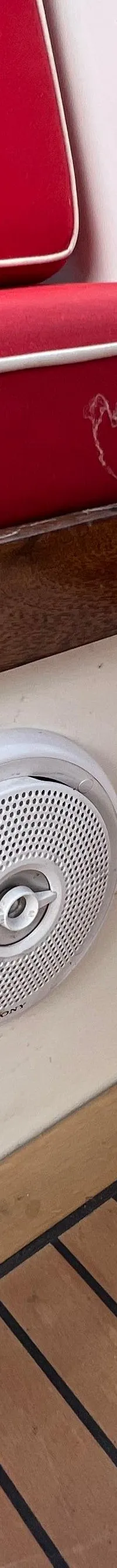 Een rode bank met witte biezen, een witte Sony-luidspreker en een houten vloer zijn zichtbaar.