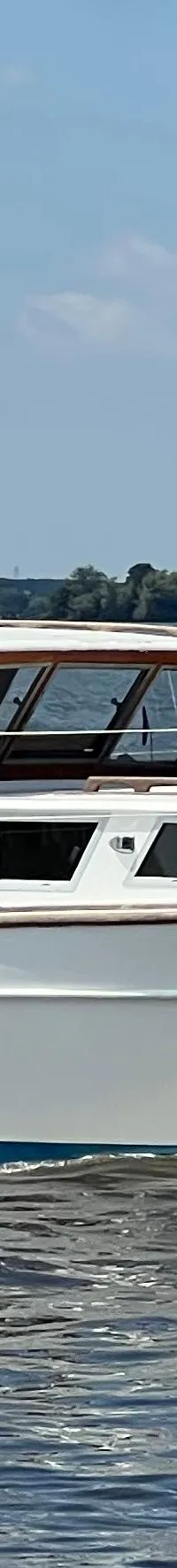 Een witte motorboot met de naam "Jenneke" vaart op een meer met een blauwe hemel en groene oevers op de achtergrond.