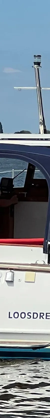 Een witte motorboot met blauwe kap en de naam "LOOSDRECHT" op de spiegel vaart op een waterweg. — Kruiser Polyflash 950