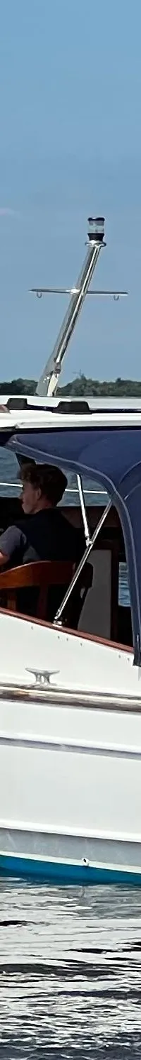 Een witte motorboot met blauwe kap en Nederlandse vlag vaart op het water, met "LOOSDRECHT" op de spiegel.