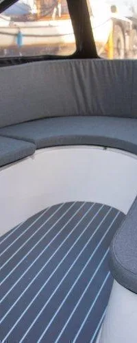 Een bootinterieur met grijze kussens op een U-vormige bank en een gestreepte vloer.