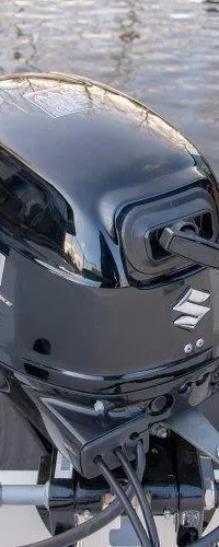 Een zwarte Suzuki buitenboordmotor is gemonteerd op de spiegel van een witte boot, met water op de achtergrond. — Clever 49