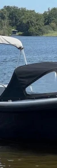 Een donkerblauwe boot met een Nederlandse vlag, een zwarte buiskap en een witte biminitop ligt in het water. — Asloep 770