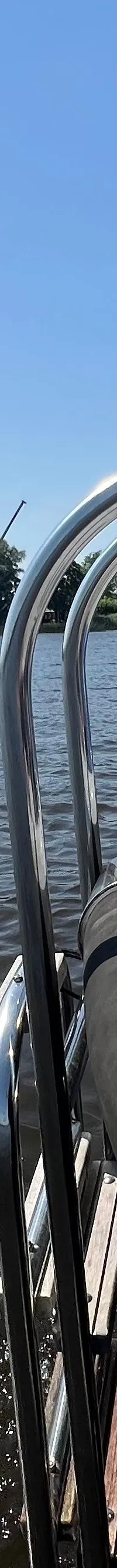 Een witte boot met een Nederlandse vlag vaart op een waterweg met bebouwing en bomen op de achtergrond. — Asloep 770